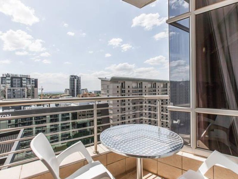 A modern apartment balcony featuring a stainless steel balustrade and tiled flooring, offering expansive urban views.
