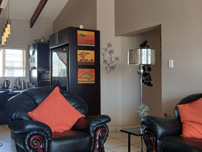 Open-plan living area featuring vaulted ceilings with exposed timber beams, tiled flooring, and an integrated kitchen with a breakfast bar.