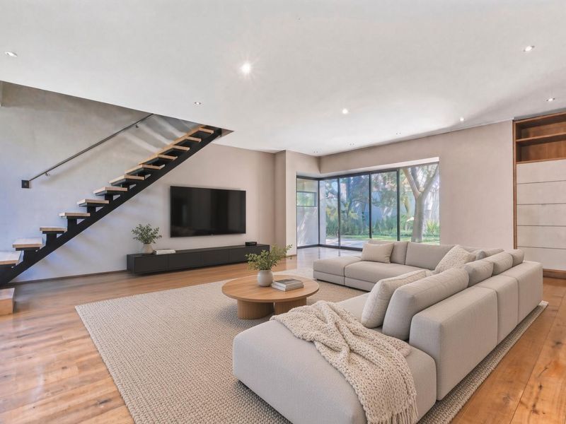 Spacious modern living room featuring hardwood floors, a striking floating staircase, built-in cabinetry, and large sliding glass doors opening to the garden.