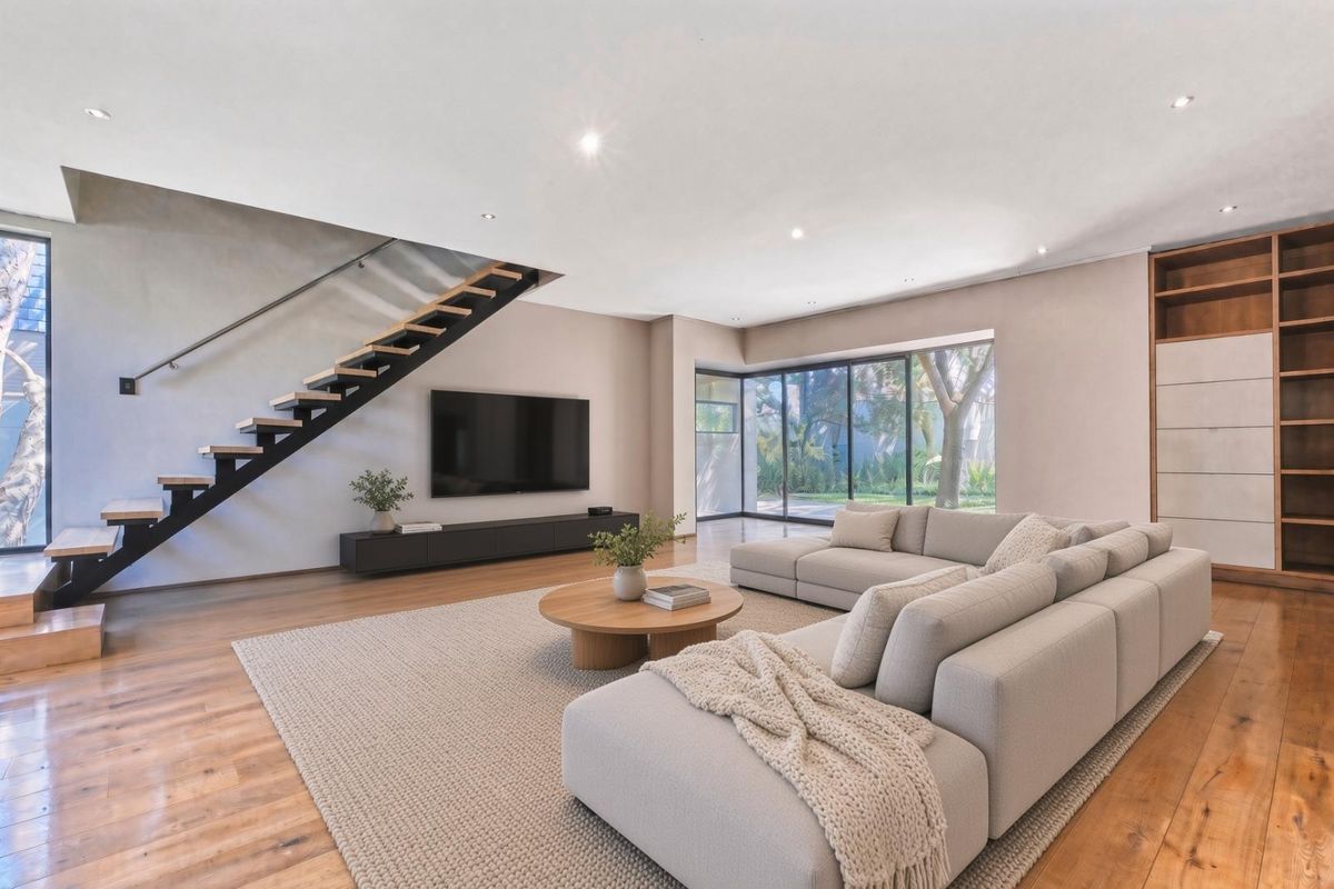 Spacious modern living room featuring hardwood floors, a striking floating staircase, built-in cabinetry, and large sliding glass doors opening to the garden.