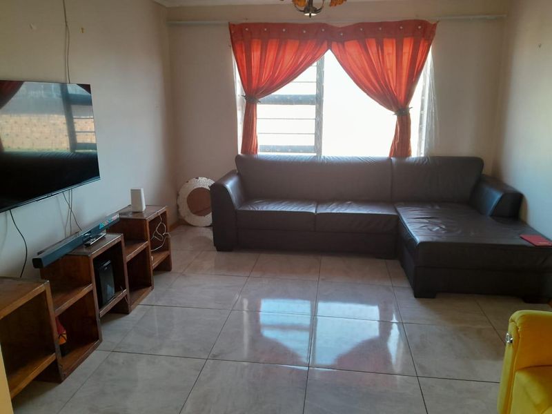 A living room featuring tiled flooring and a window with security bars, offering a functional space for relaxation.