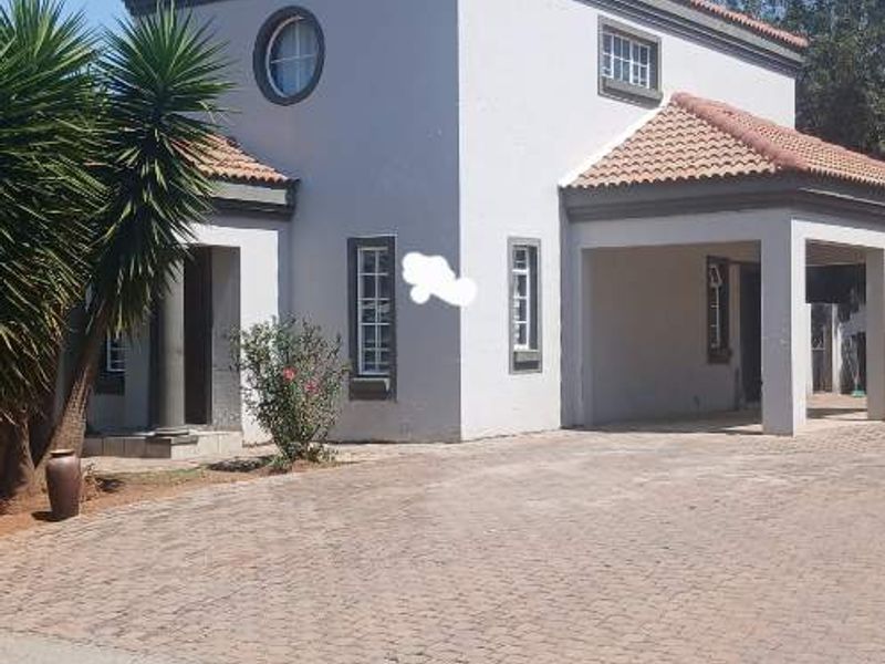 Front elevation of a townhouse featuring a paved driveway, covered carport, and classic terracotta roof tiles.