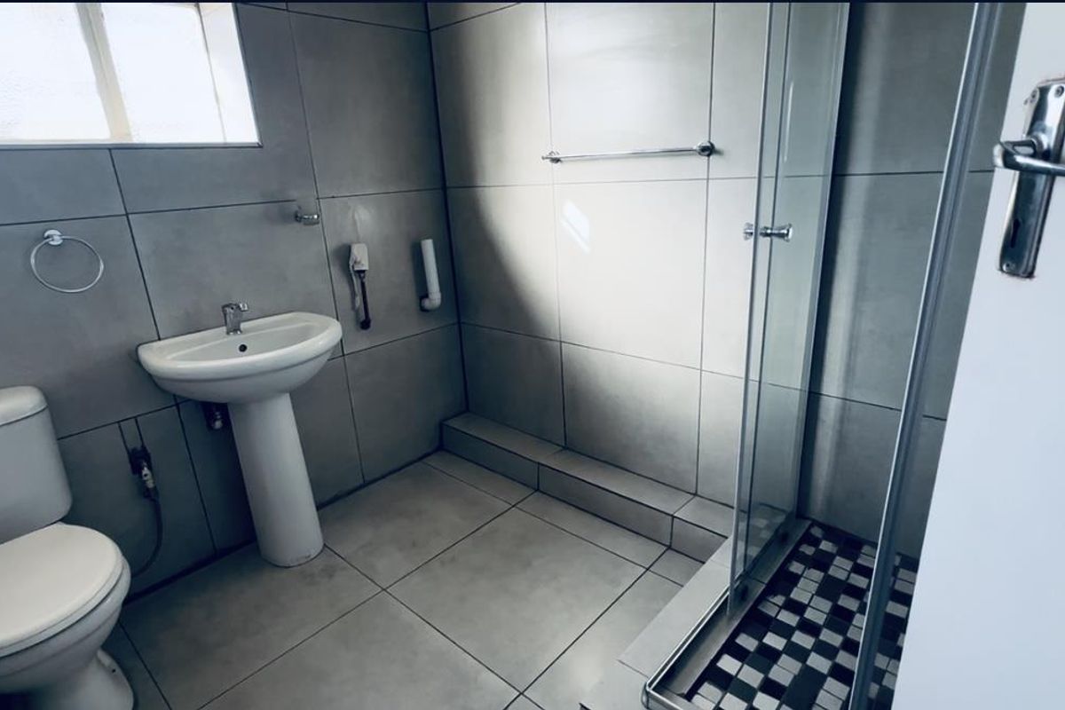 A functional bathroom featuring a pedestal basin, toilet, and a glass-enclosed shower with tiled finishes throughout.