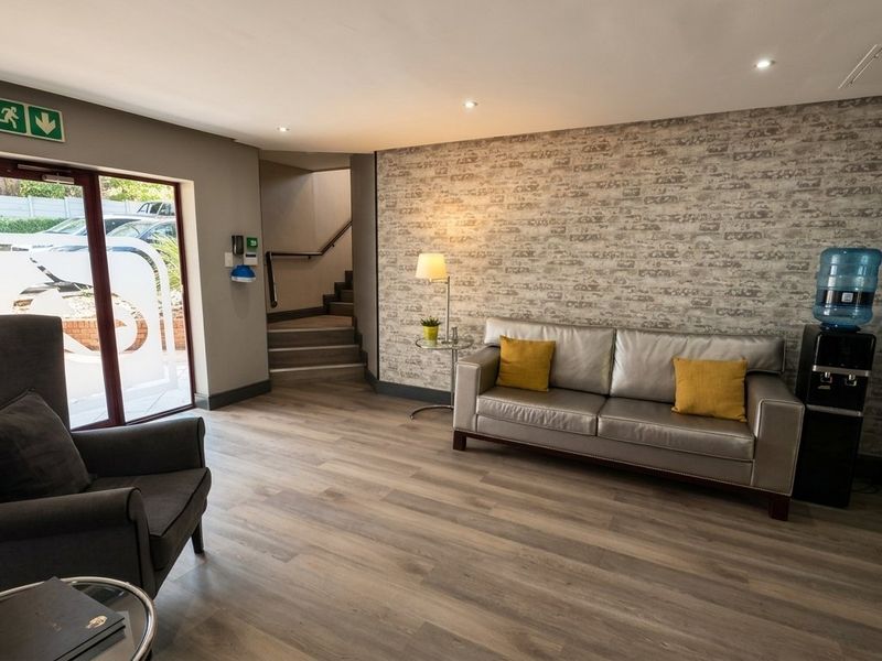 A well-maintained commercial reception or entry area featuring laminate flooring, recessed lighting, and a staircase leading to an upper level.