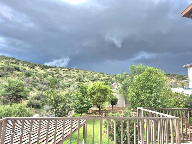 Scenic elevated view overlooking a landscaped garden and natural hillside terrain, framed by a metal balcony railing.
