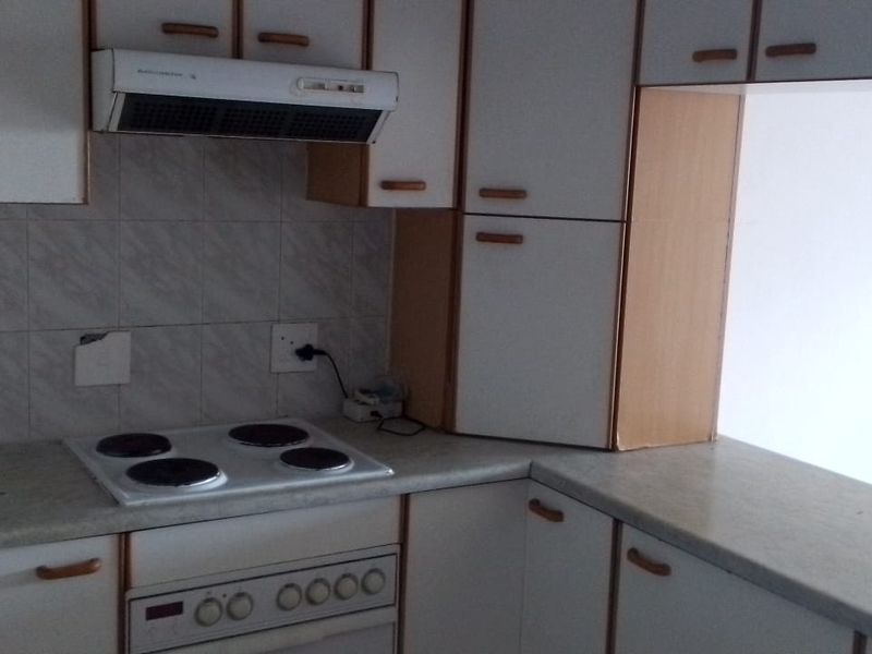 A dated kitchen featuring white cabinetry, laminate countertops, and built-in electric cooking appliances, offering a functional layout ready for modernization.