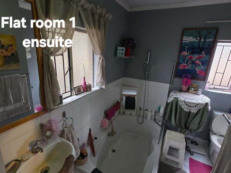 Ensuite bathroom featuring a built-in bathtub, pedestal basin, and toilet, with tiled splashbacks and security bars on the windows.