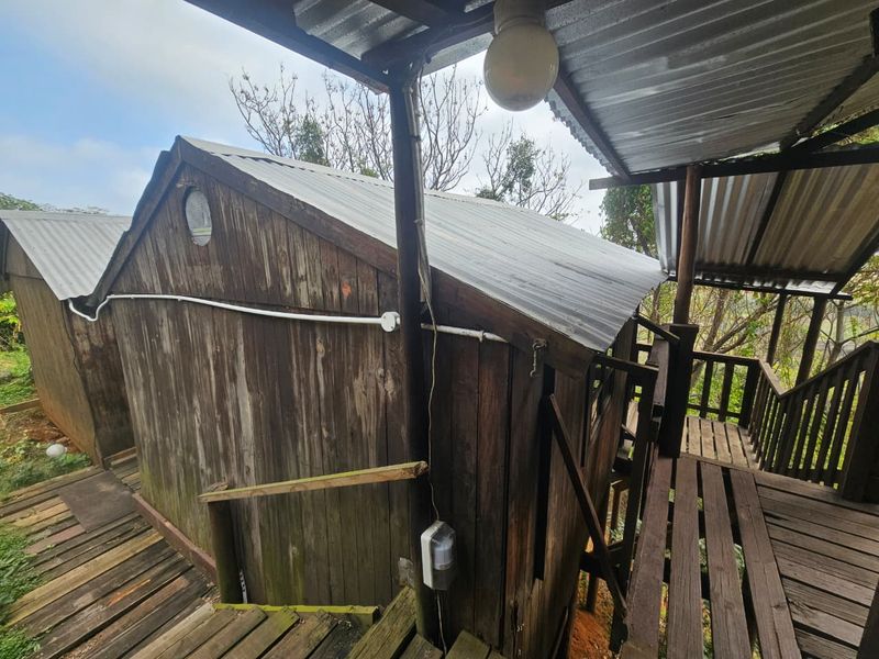 Exterior view of a rustic timber structure featuring corrugated metal roofing and elevated wooden decking, showing significant signs of weathering and wear.