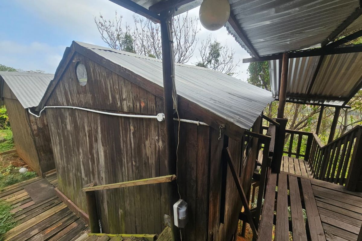 Exterior view of a rustic timber structure featuring corrugated metal roofing and elevated wooden decking, showing significant signs of weathering and wear.
