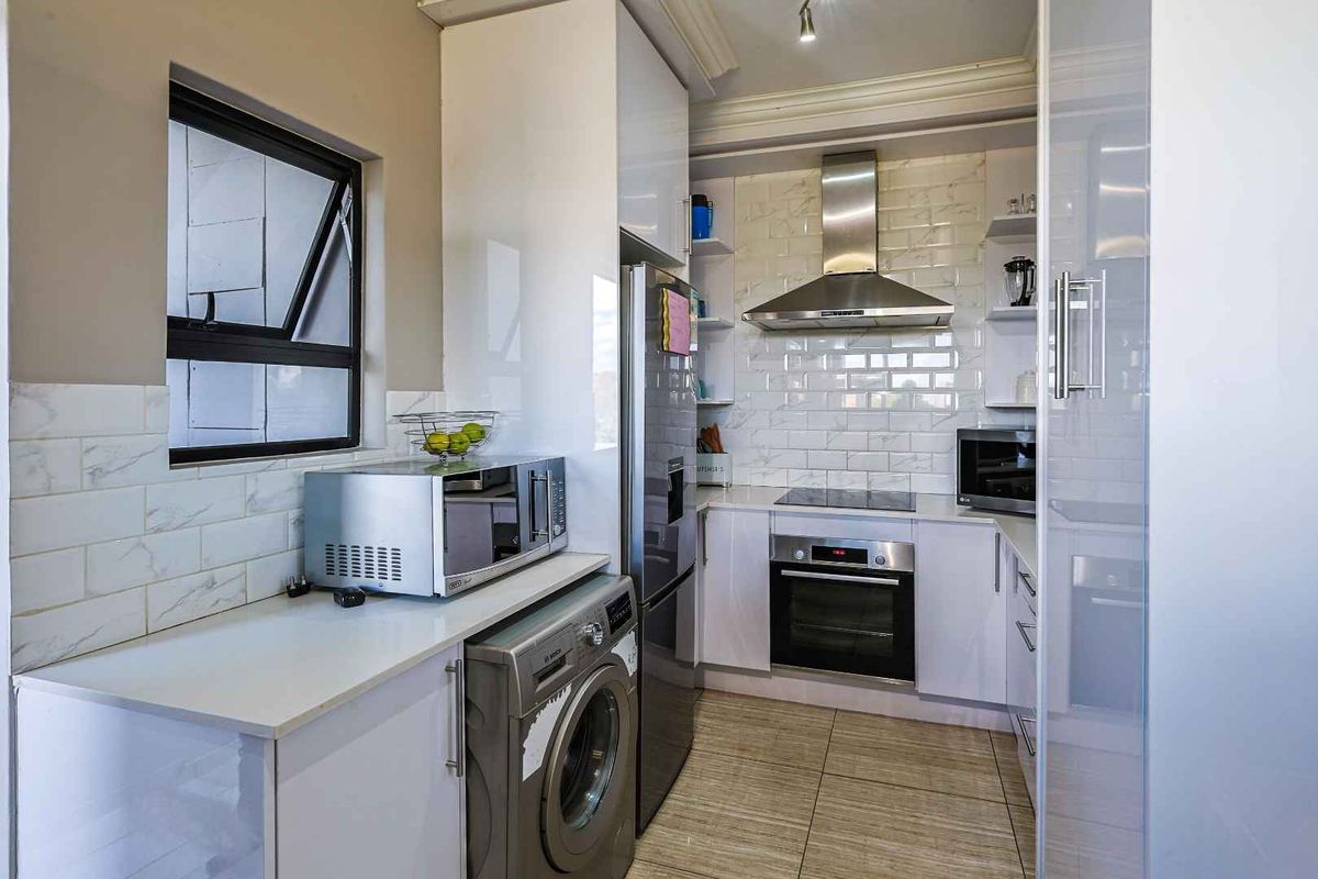Modern compact kitchen featuring white cabinetry, marble-look subway tile backsplash, stainless steel extractor fan, built-in oven, and integrated laundry appliance space.