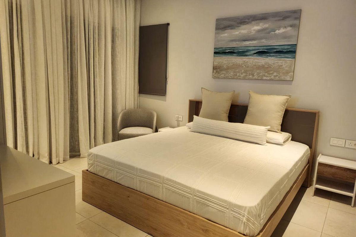 A well-maintained bedroom featuring neutral tiled flooring, floor-to-ceiling curtains, and integrated electrical outlets, offering a clean and comfortable living space.