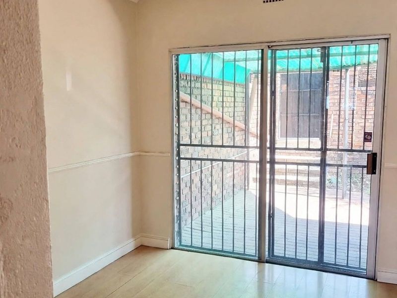 An empty living area featuring laminate flooring, a ceiling fan, and sliding glass doors with security gates leading to an outdoor patio space.