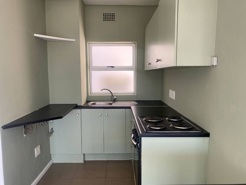 A compact kitchen featuring built-in cabinetry, laminate countertops, a stainless steel sink, and an integrated electric hob and oven.