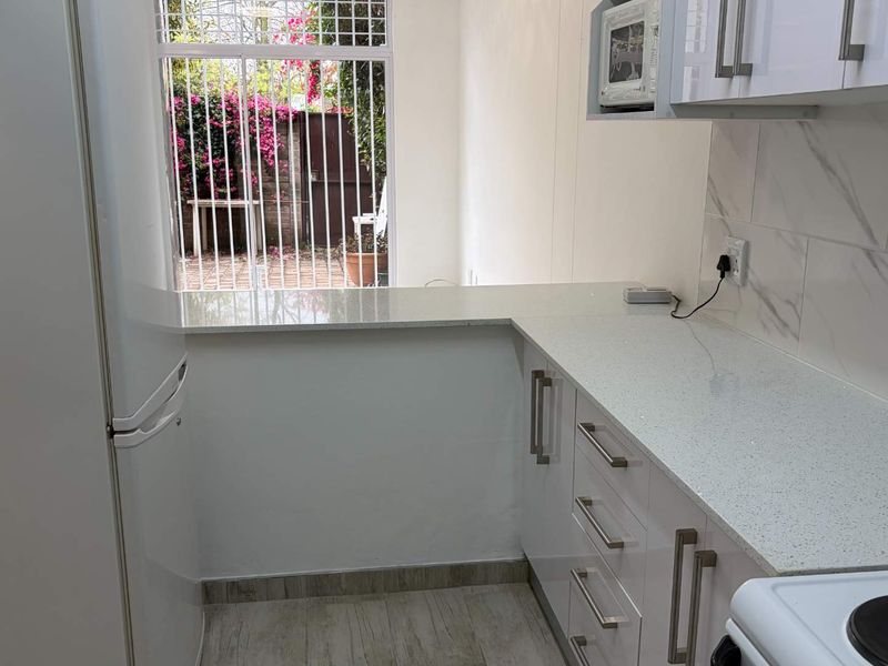 Modern kitchen featuring white cabinetry, quartz countertops, marble-look backsplash, and a built-in microwave, with a window overlooking the exterior.