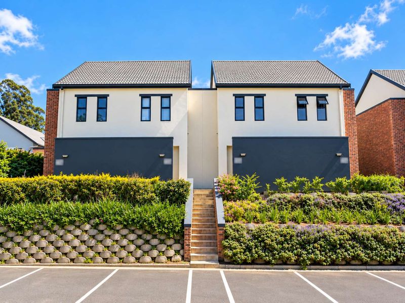Modern two-story duplex facade featuring a central concrete staircase, landscaped retaining walls, and contemporary exterior finishes with dedicated parking bays.