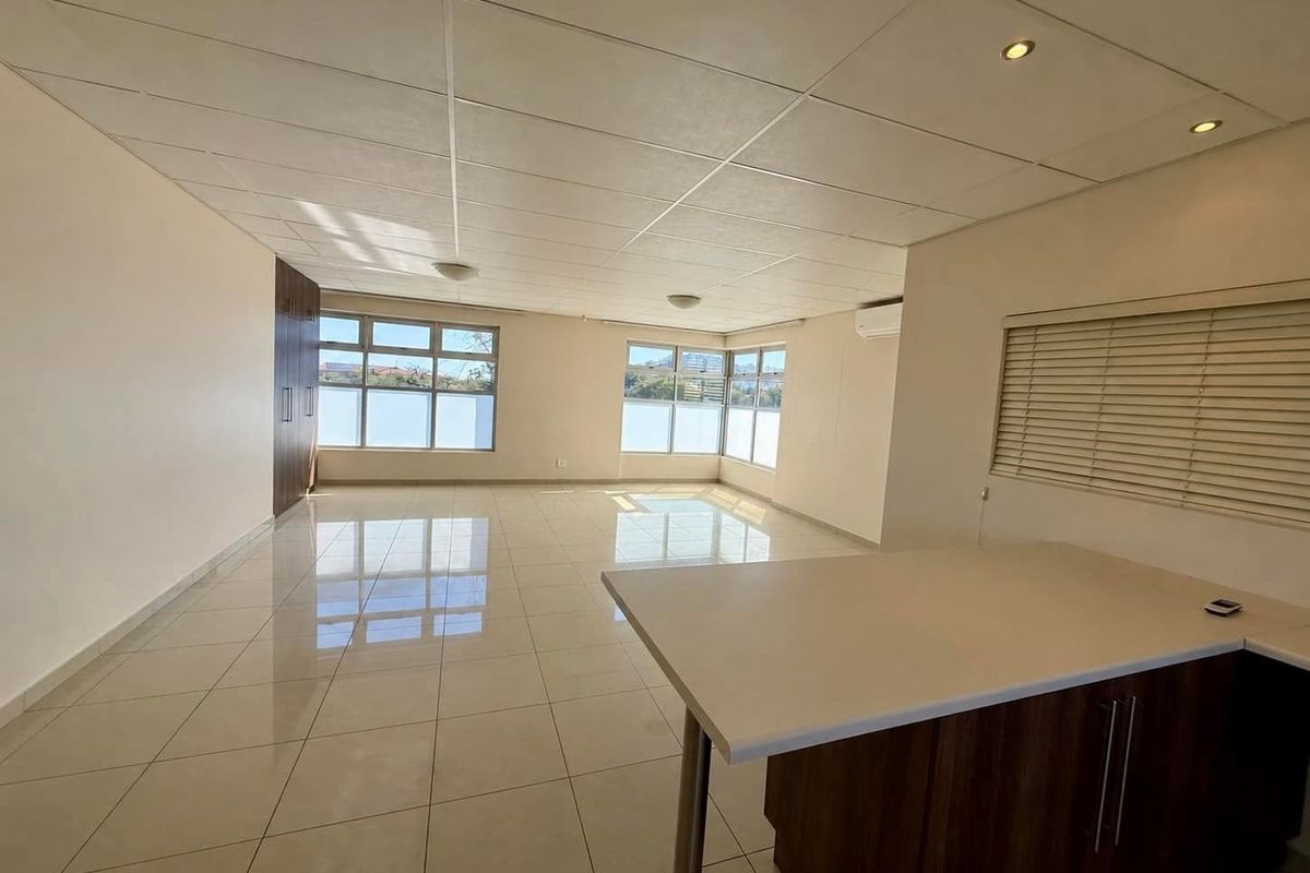 Spacious open-plan living area featuring polished tile flooring, a modern kitchen island, drop ceiling with recessed lighting, and large windows with venetian blinds.