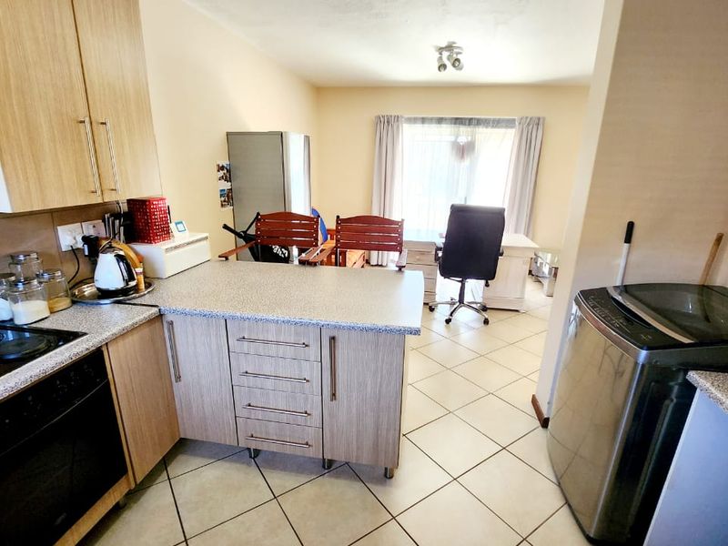 Open-plan kitchen and living area featuring light wood-finish cabinetry, laminate countertops, built-in oven and hob, and tiled flooring throughout.