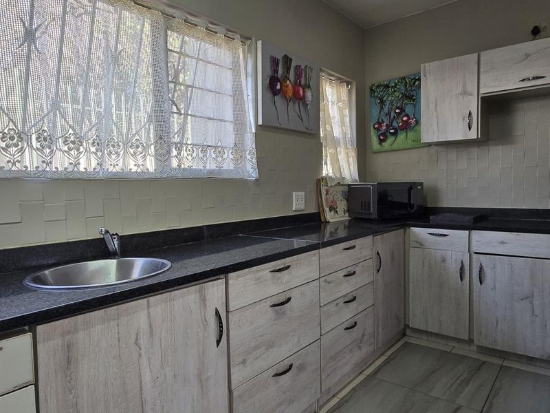 A functional kitchen featuring light wood-look cabinetry, dark stone countertops, a stainless steel sink, and tiled backsplash with security bars on the windows.