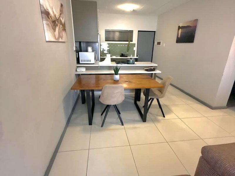 An open-plan living and kitchen area featuring neutral tiled flooring, modern cabinetry, and a functional breakfast bar layout.