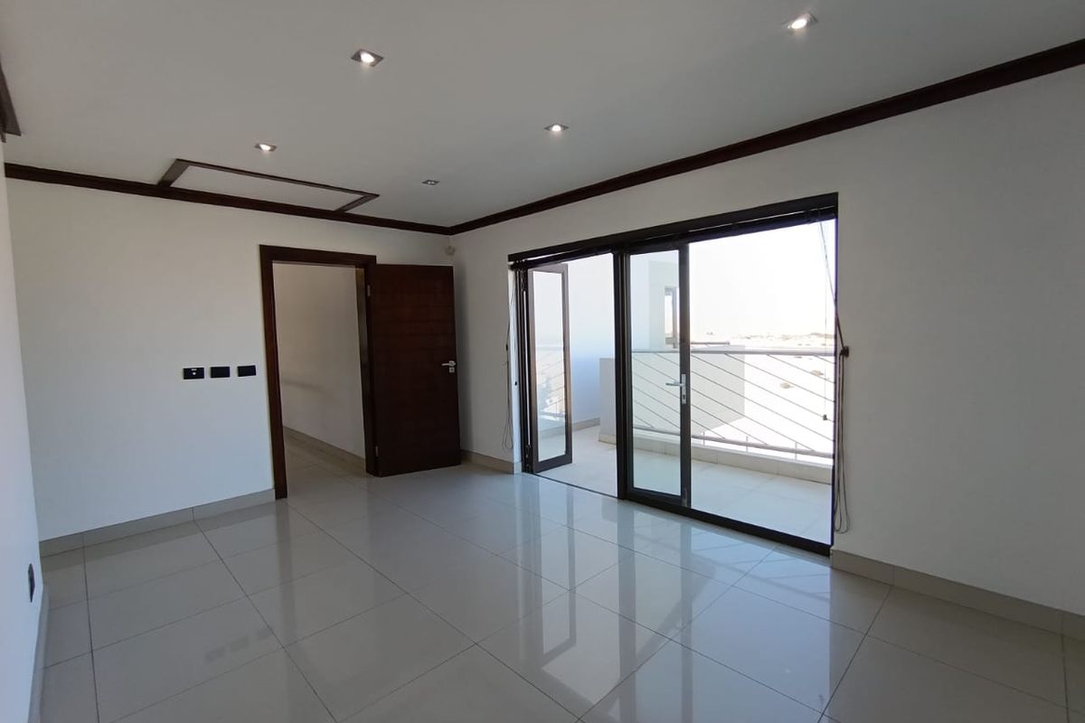 Bright living room featuring large sliding glass doors leading to a balcony, tiled flooring, recessed ceiling lighting, and dark wood door frames.