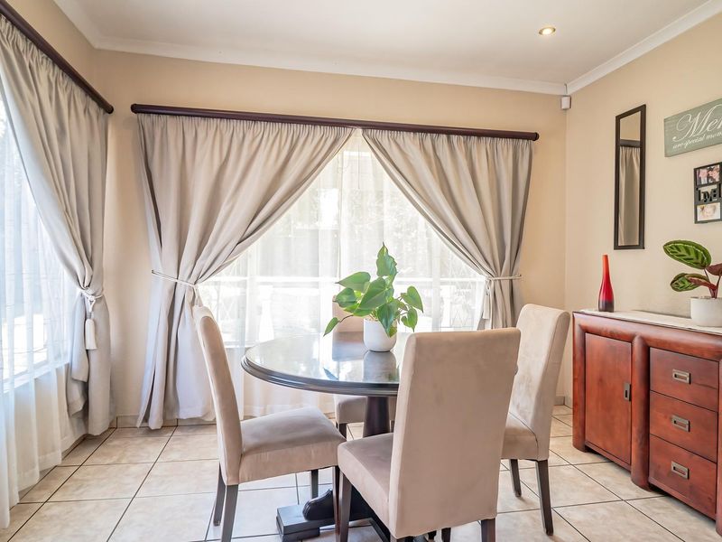 A bright and well-maintained dining area featuring neutral tiled flooring, large windows with curtains, and recessed ceiling lighting.