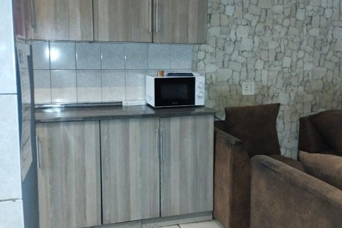 A compact kitchen area featuring wood-look cabinetry, tiled backsplash, and a distinctive stone-cladding feature wall, seamlessly integrated into the living space.