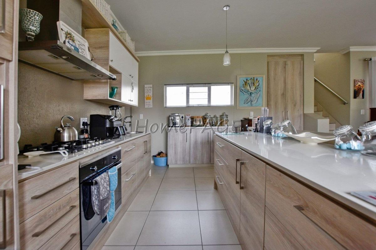 Modern kitchen featuring light wood cabinetry, stone countertops, a central island, built-in oven, gas hob, and extractor fan with tiled flooring.