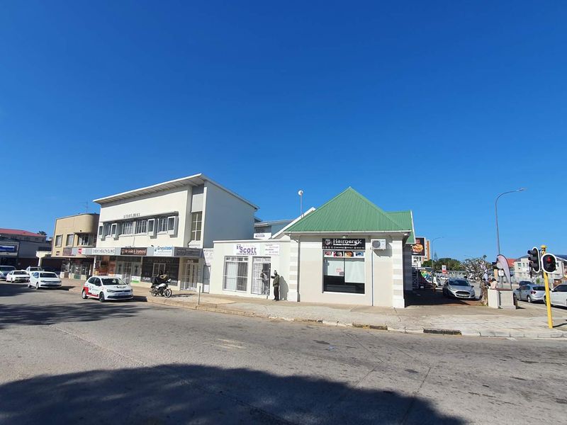 Street-level view of a mixed-use commercial property featuring multiple storefronts, paved sidewalks, and traffic infrastructure in a busy urban setting.