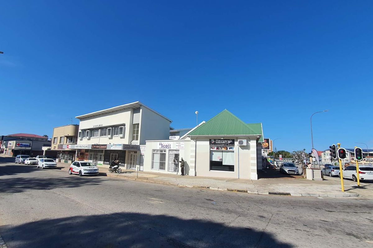 Street-level view of a mixed-use commercial property featuring multiple storefronts, paved sidewalks, and traffic infrastructure in a busy urban setting.