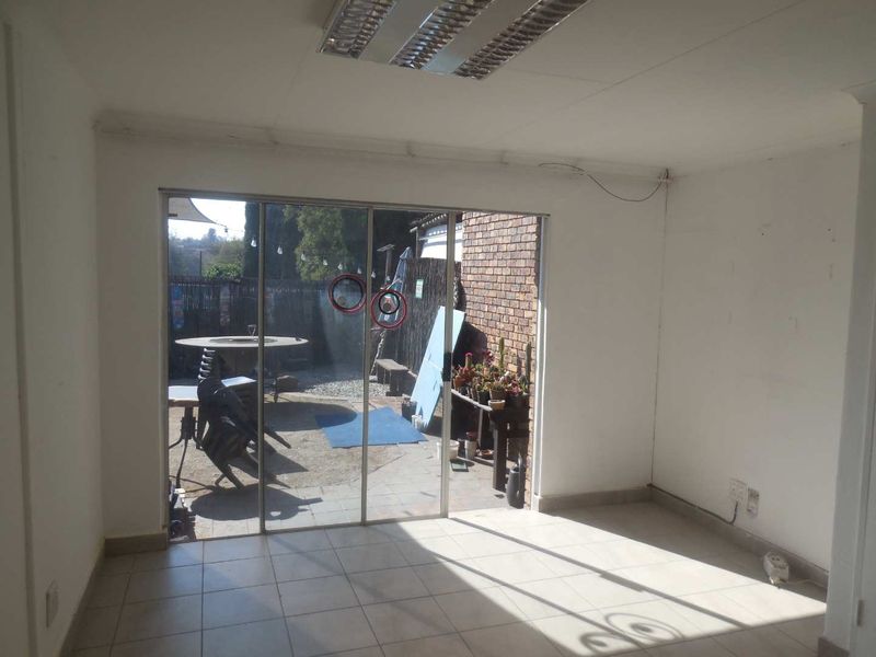 An empty office space featuring tiled flooring, a fluorescent ceiling light, and a sliding glass door providing access to an outdoor area.