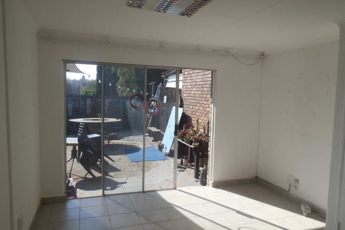 An empty office space featuring tiled flooring, a fluorescent ceiling light, and a sliding glass door providing access to an outdoor area.