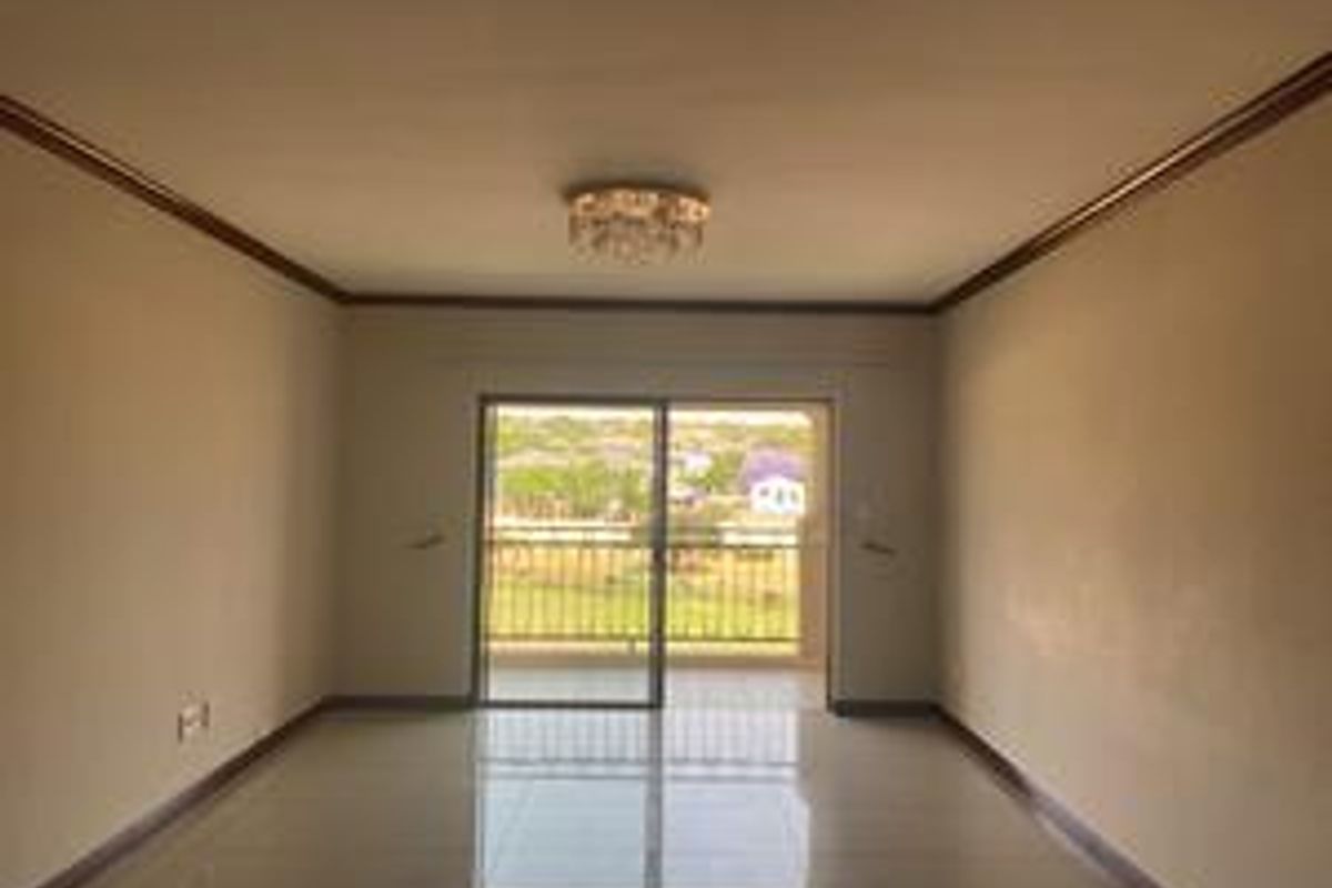 A spacious, empty living area featuring tiled flooring, crown molding, and a sliding glass door leading to a balcony with scenic views.