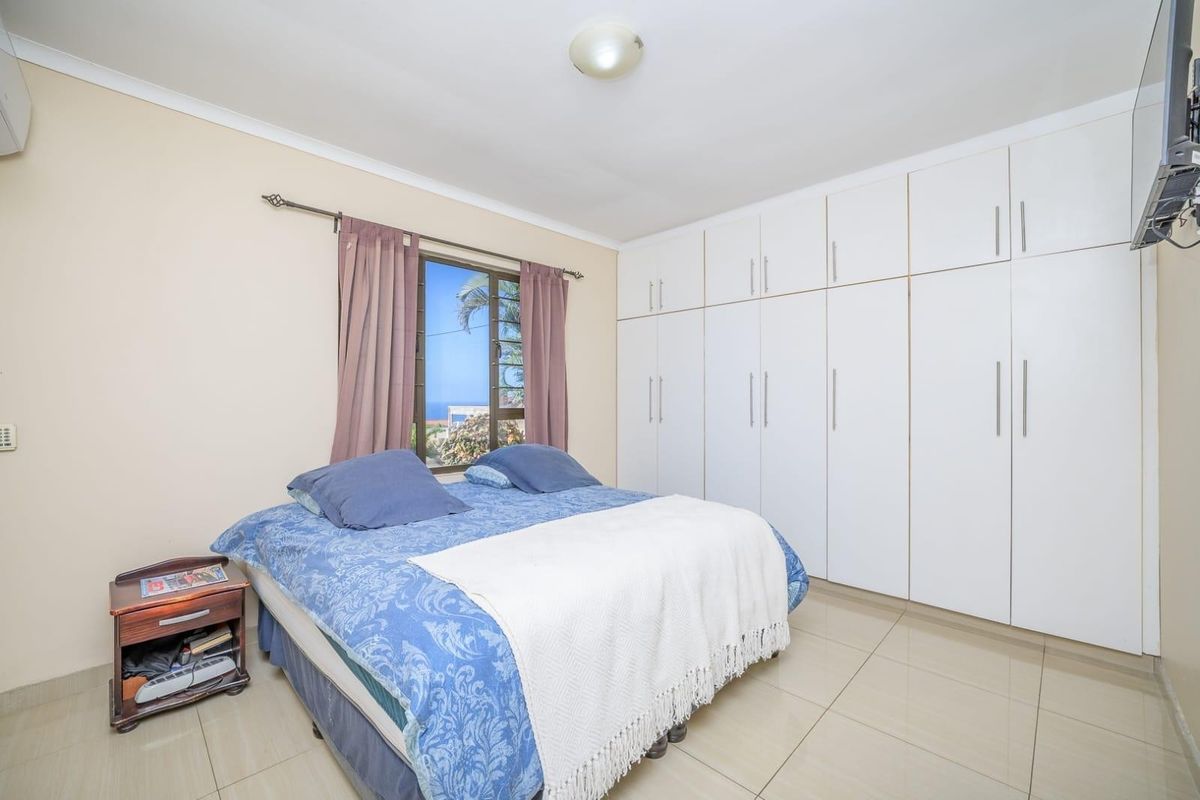 A well-maintained bedroom featuring extensive built-in white cabinetry, tiled flooring, and a wall-mounted air conditioning unit.