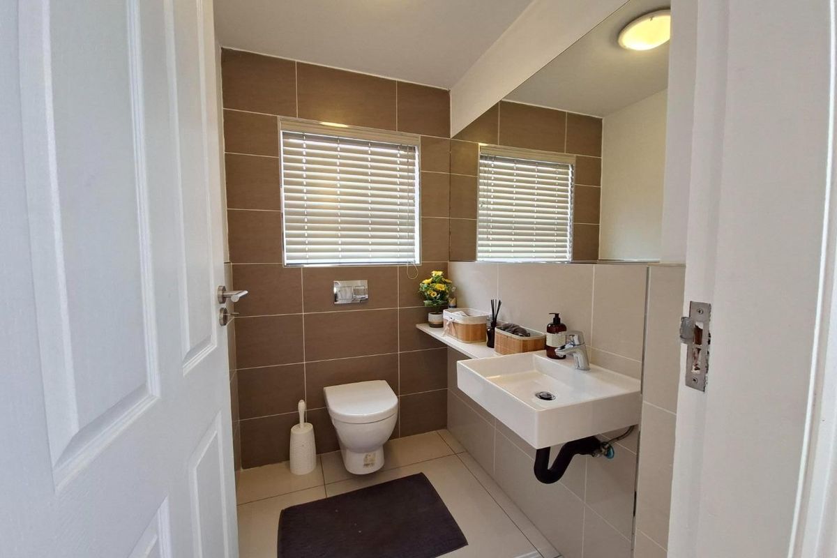 A modern, compact bathroom featuring a wall-hung toilet with concealed cistern, a wall-mounted basin, and large wall mirror with neutral tiled finishes.