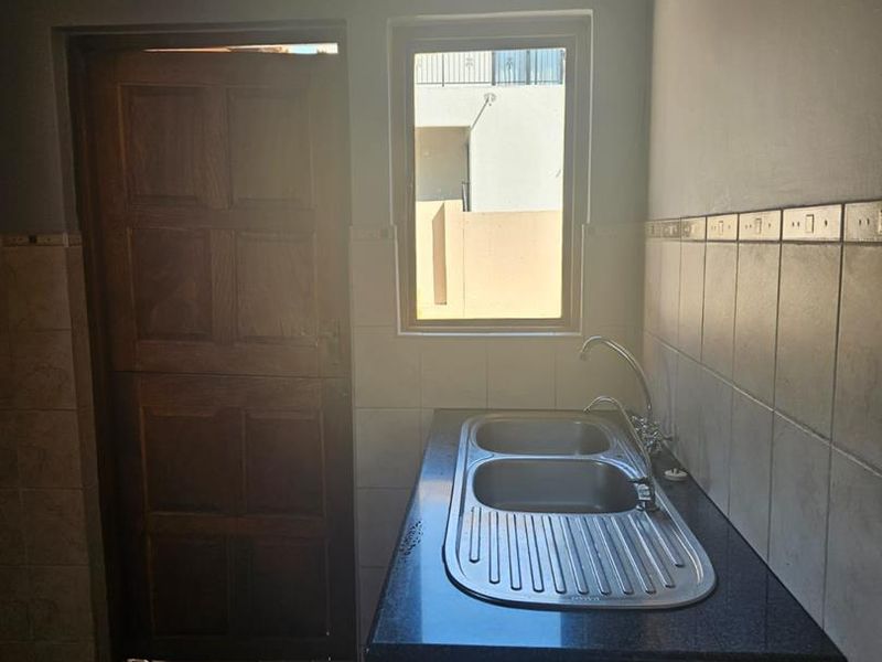 A functional scullery area featuring a double bowl stainless steel sink, granite countertops, and tiled splashbacks, providing a practical space for kitchen prep.