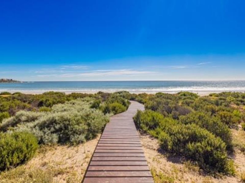 A scenic wooden boardwalk path leading through coastal dunes towards the ocean, offering direct beach access and expansive sea views.