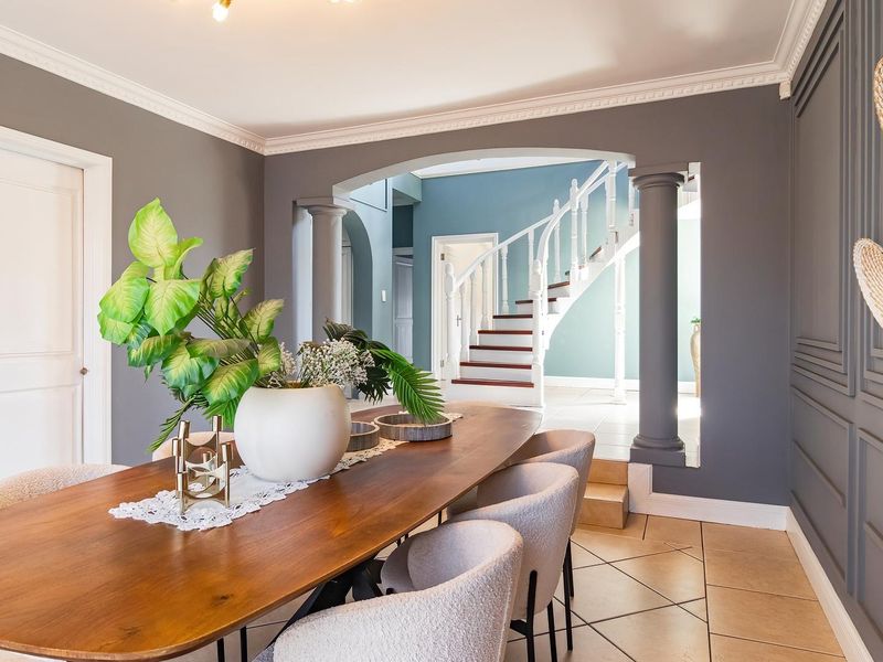 Elegant dining room featuring decorative wainscoting, crown molding, and a grand arched opening leading to a staircase with classic balustrades.