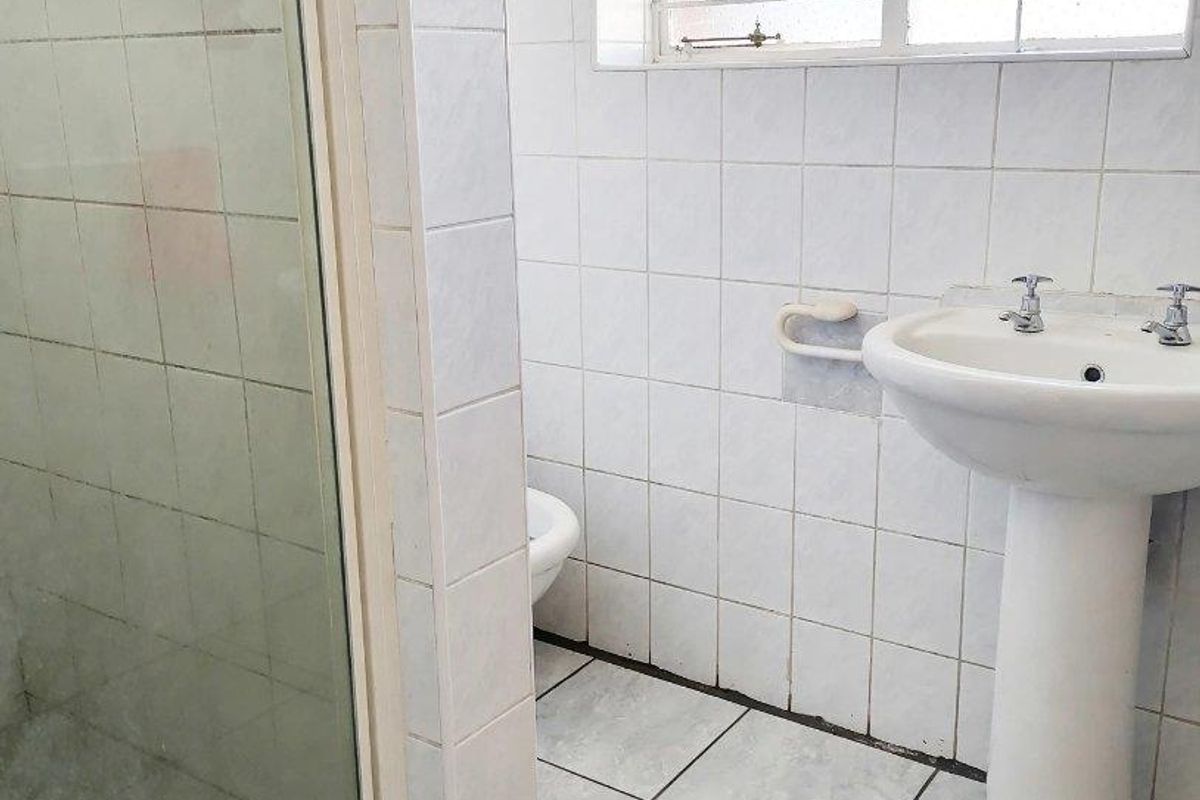 A dated bathroom featuring a pedestal washbasin, shower enclosure, and white ceramic tiling throughout.