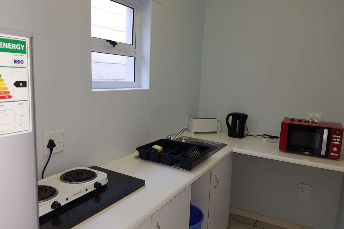 A compact kitchenette featuring white cabinetry, a stainless steel sink, and a countertop with a portable electric stove.