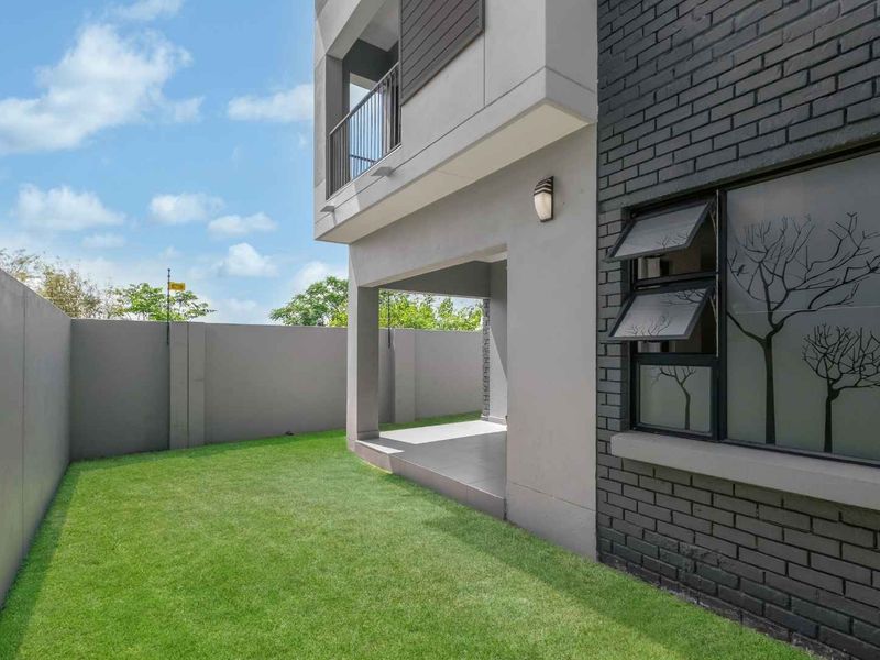 A well-maintained rear exterior view featuring a private garden, a covered patio area, and modern brick and plaster facade finishes.