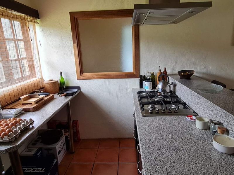 A functional kitchen featuring granite countertops, a gas hob with an overhead extractor fan, and tiled flooring with a timber-framed window.
