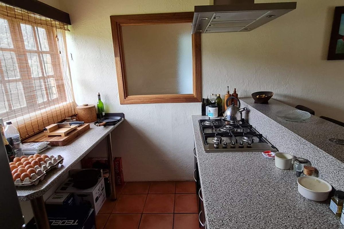 A functional kitchen featuring granite countertops, a gas hob with an overhead extractor fan, and tiled flooring with a timber-framed window.