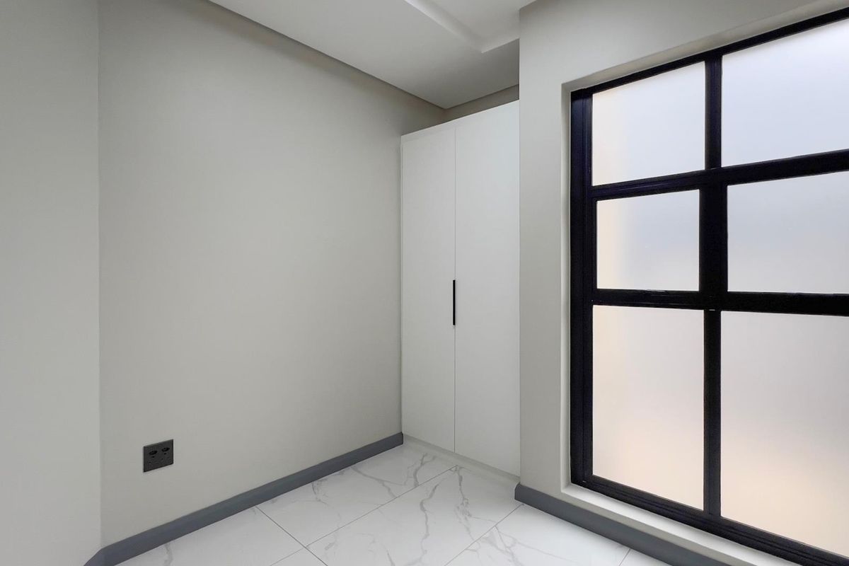 A clean, modern bedroom featuring built-in wardrobes, large frosted glass windows with black frames, and elegant marble-look floor tiles.