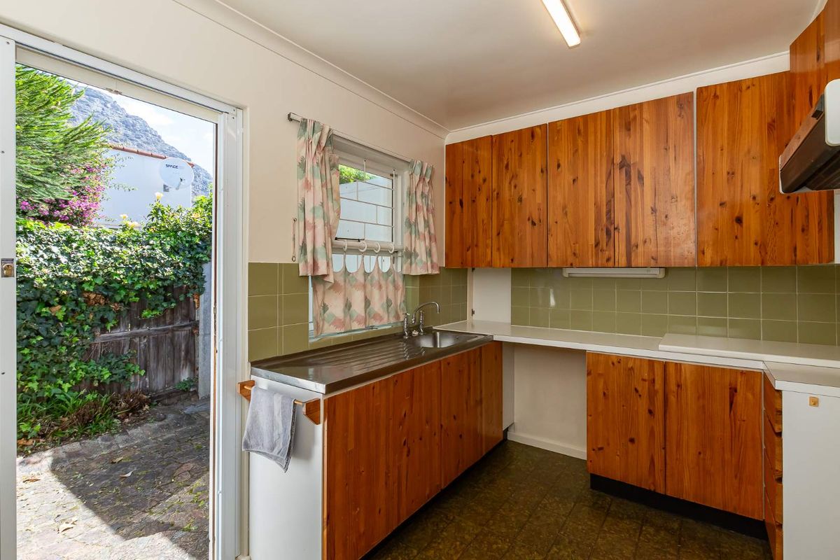 A dated kitchen featuring timber cabinetry, a stainless steel sink, and direct access to an outdoor patio area.