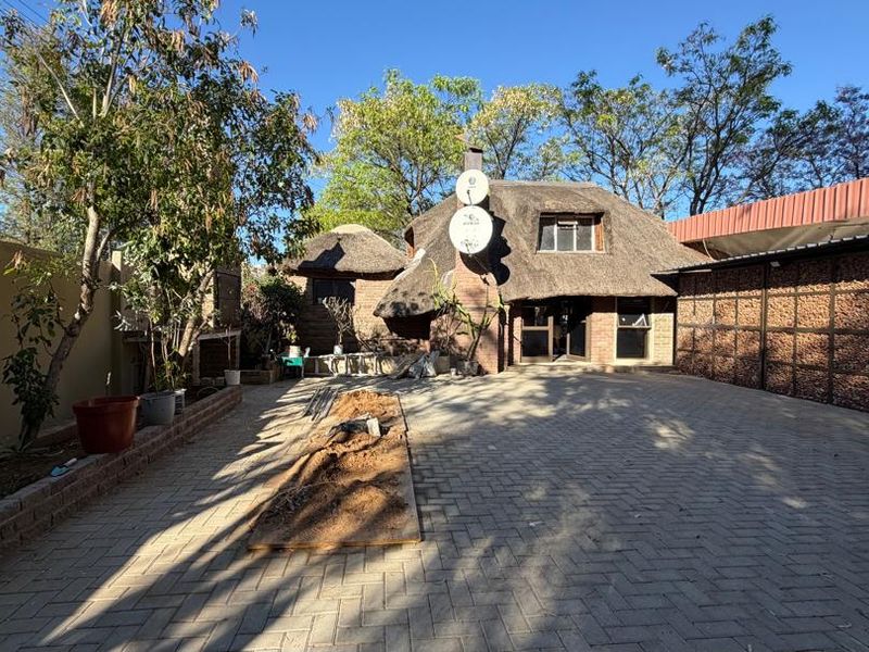 Front exterior view of a property featuring a traditional thatch roof, brick paved driveway, and stone-clad boundary wall.