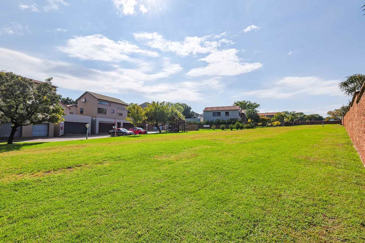 A wide-angle view of a communal green space and lawn area within a townhouse complex, featuring surrounding residential units and boundary walls.