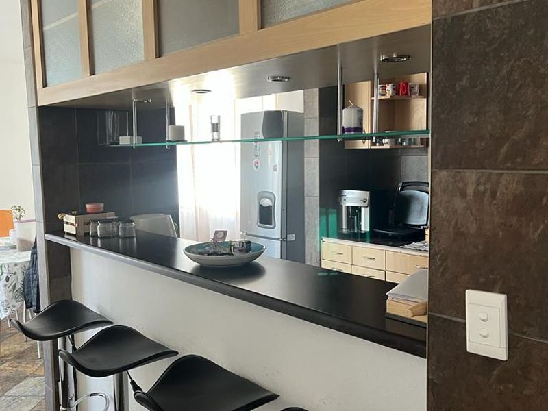 A kitchen area featuring a breakfast bar with dark countertops, tiled wall accents, and built-in cabinetry with glass-fronted overhead storage.
