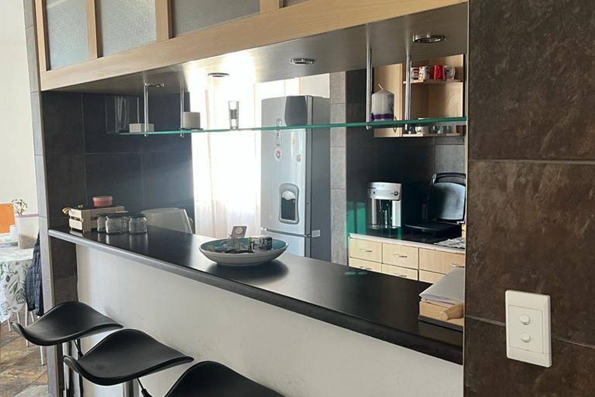 A kitchen area featuring a breakfast bar with dark countertops, tiled wall accents, and built-in cabinetry with glass-fronted overhead storage.