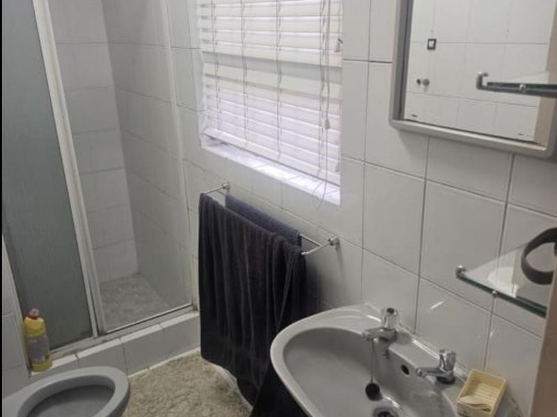 A functional bathroom featuring a shower enclosure, pedestal basin, and tiled finishes throughout.