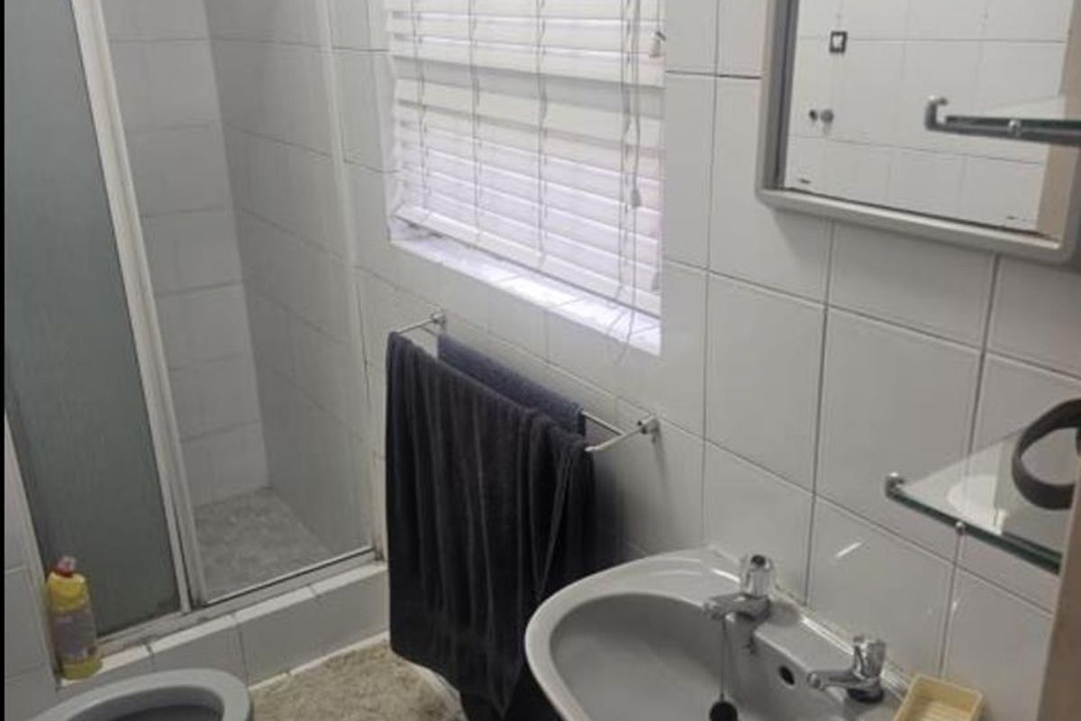 A functional bathroom featuring a shower enclosure, pedestal basin, and tiled finishes throughout.